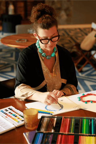 Woman drawing with colored pencils at a table in a cozy room.