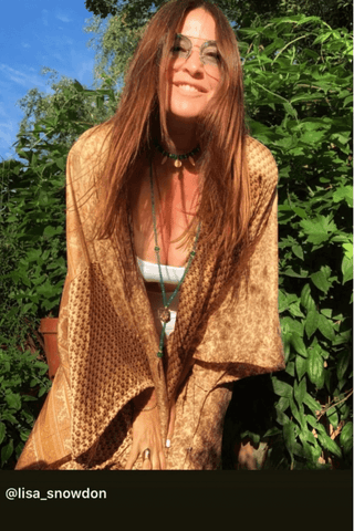 Person wearing a brown quilted jacket sitting outdoors with greenery in the background