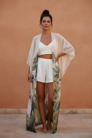 Woman wearing a white outfit with a long, light-colored cover-up against a peach-colored wall.