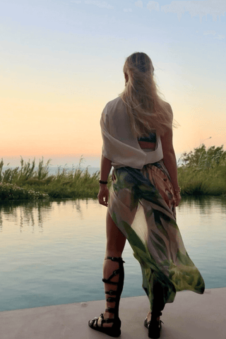Person standing by a body of water with a colorful scarf and white top