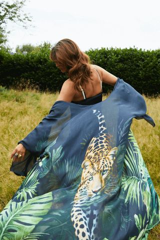 Woman holding a large blue scarf with a leopard design in a grassy field.
